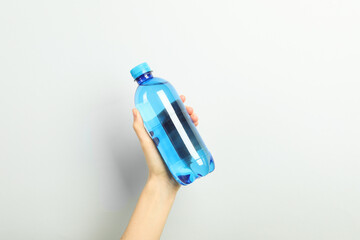 Wall Mural - Woman holding plastic bottle of water on light background, closeup