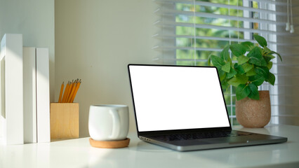 Fototapete - Modern workspace setup with a laptop, coffee mug, and a green plant by the window, illuminated by natural light.