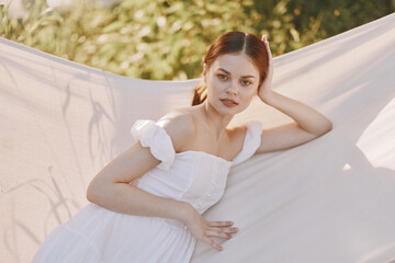 Wall Mural - A serene young woman wearing a white dress poses gracefully against a soft natural backdrop, evoking tranquility and elegance in a bright, sunny setting