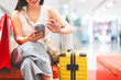© dodotone - Woman hand using smartphone sitting with travel luggage indoors shopping department store
