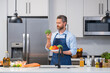 © Volodymyr - Portrait of chef man in cook apron with a plate of vegetable salad in the kitchen. Man cooking vegan healthy salad in kitchen. Millennial man at modern kitchen with vegetables, prepare fresh vegetable