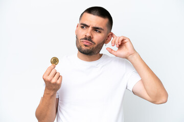 Young caucasian man holding a bitcoin isolated on white background having doubts