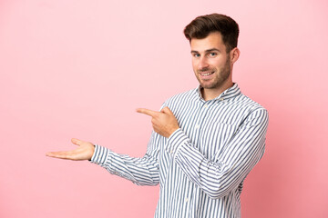 Wall Mural - Young caucasian handsome man isolated on pink background holding copyspace imaginary on the palm to insert an ad