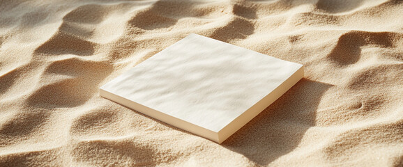 Poster - A blank white sheet of paper resting on golden sand, with soft lighting and gentle textures, symbolizing creativity, free space for writing, and design mockups in a natural environment.