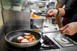 © pavel siamionov - A chef skillfully cooks meat pieces in a frying pan on an induction stove, showcasing a professional kitchen setting.