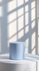 Aufkleber - A pastel blue cylinder podium stands gracefully atop a smooth surface, casting delicate shadows against a sunlit wall, enhancing the serene ambiance of the room