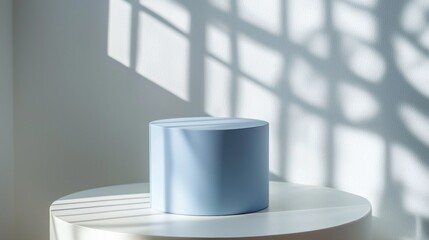 Aufkleber - A pastel blue cylinder podium stands elegantly on a white table, surrounded by soft sunlight pouring through shadows, evoking tranquility and style in a minimalist decor setting