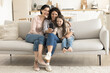 © fizkes - Digital fun. 3 female generations senior grandma grownup mom small child girl relax on couch together hug use cellphone to play game online make videocall text funny message in family chat. Copy space