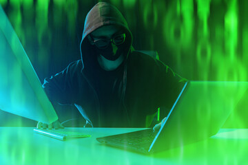 Poster - Man cyber criminal with computers. Hacker hides face under mask and hood. Cyber scammer with laptop and monitor. Hacker near green binary code. Man cyber villain develops viruses.