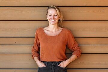 Wall Mural - A woman in an orange sweater is smiling and standing in front of a wooden wall. The image conveys a warm and friendly atmosphere, with the woman's smile