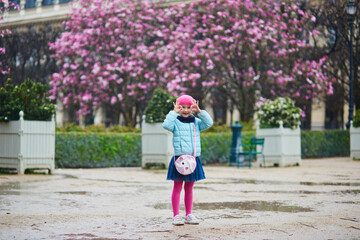 Wall Mural - Adorable preschooler girl enjoying pink magnolias in full bloom on a rainy day in a park of Paris, France