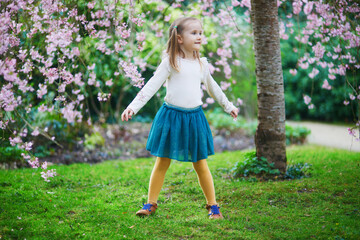 Wall Mural - Adorable preschooler girl enjoying nice spring day in park during cherry blossom season