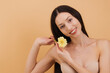 © anatoliycherkas - Beautiful smiling woman holding yellow gerbera flower near face on a beige background.