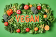 © Tatsiana - Fresh vegetables and fruits arranged artistically with vegan text on a vibrant green backdrop for a joyful plant-based lifestyle