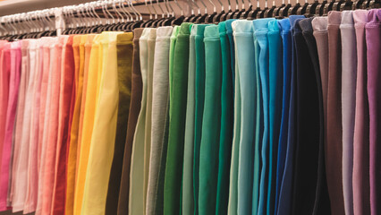 Poster - A rack of colorful pants with a rainbow of colors. The pants are hanging on a rack and are of various colors