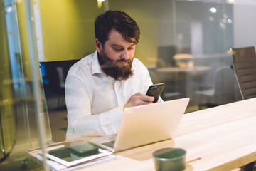 Wall Mural - Handsome executive browsing mobile and using laptop in workplace