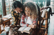 © simona - Happy couple enjoying tender moment at home, woman with curly hair sitting at table reading book while man with beard stands behind her, embracing her with warmth and affection during relaxing morning