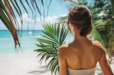 Wall Mural - Beautiful woman in light-colored beachwear holding a palm leaf, with a tropical island background