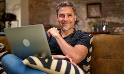 older man working online with laptop computer at home sitting on couch in living room. home office, 