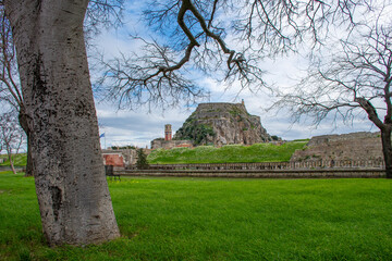 Wall Mural - Verdant field framing an ancient fortress perched atop a rocky hill, beneath a sky brushed with clouds.