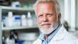 © Iona - A bearded scientist in a white lab coat smiles confidently in a lab filled with scientific equipment and shelves.