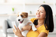 © Prostock-studio - Happy young asian woman in casual sitting on floor in living room, taking selfie with her playful cute dog jack russel terrier puppy while playing together at home, using mobile phone, copy space