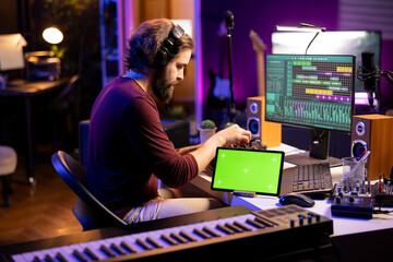 Fototapete - Professional artist editing audio recordings on daw software interface, working on music industry post production next to greenscreen on tablet. Young musician mixing and mastering tunes at home.