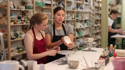 Wall Mural - Female potter teaches young apprentices how to make pottery on potter wheel in a workshop. High quality 4k footage