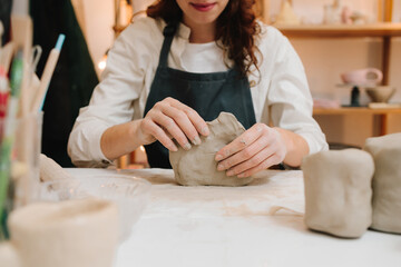 Poster - Potter is sculpting wet clay for ceramics products. Hands of a female potter making ceramic clay product on the table in the pottery workshop.