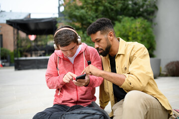 Wall Mural - Happy young man with Down syndrome and mentoring friend sitting and talking outdoors, spending time together.