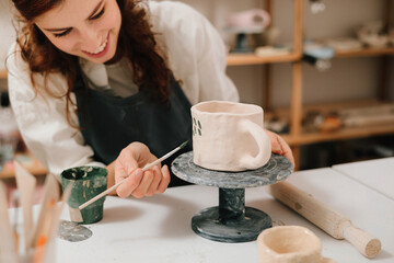 Poster - Process of designing cup with a traditional pattern in pottery art studio. Artisan stamps decorative symbols on the dry clay of the cup.