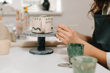 Poster - Painter is drawing and adding unique designs to the earthenware. Artist is decorating and painting handmade ceramic clay cup in the creative workshop.