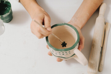 Poster - Female artist is painting earthenware with paintbrush and water colors in the workshop. Painter is drawing and making a colorful decoration of a clay ware.