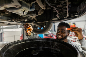 Fototapete - Close up of interracial auto mechanic changing oil on car at car service.
