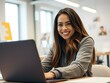 © LooPanda-Pictures - Smiling Woman in Modern Office: A young, smiling woman with long brown hair is shown in a modern office setting, working on her laptop, radiating professional warmth and focused determination.