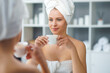 © Acronym - Young Girl is Sitting in front of a Make-up Mirror in the Bathroom and Applying a Skin Cream. Beautiful Woman is Making Cosmetic Rejuvenation Procedures.