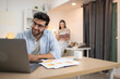 © Wosunan - Portrait of a young freelancer smiling while working online via laptop at home with his girlfriend