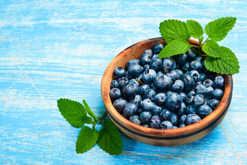 Wall Mural - Blueberries in a wooden bowl. Top view, on a blue wooden background. Berries close-up.