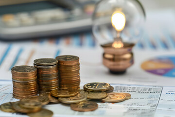 Poster - Stacked coins beside a glowing lamp on financial documents with graphs and a calculator in background