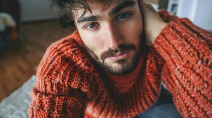 Wall Mural - Young man in cozy orange sweater posing for a close-up shot in a softly lit indoor setting