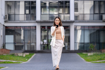 A woman is walking down a sidewalk with a cell phone in her hand