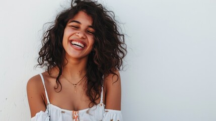 Wall Mural - Joyful young woman with curly hair smiles brightly against a simple white background, radiating happiness and positivity