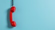 © crispy - Red vintage telephone handset hanging on plain blue wall. Retro communication device against pastel background. Classic design element with empty space for text