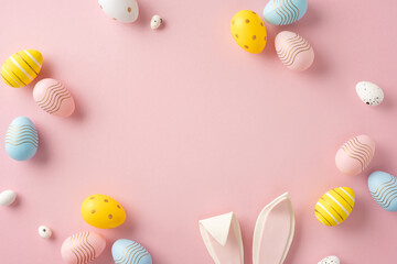 Wall Mural - easter-themed flat lay featuring colorful painted eggs with bunny ears on pink background
