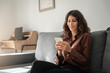 © Stock 4 You - Young freelance business woman sitting on couch sofa using mobile phone application for work remotely, chatting online. Latin hispanic girl holding gadget in apartment home with cozy modern interior