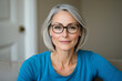 © Sunny Good Cat - middle aged woman with short gray hair and glasses is sitting indoors, wearing blue shirt. She has calm and confident expression, creating warm atmosphere