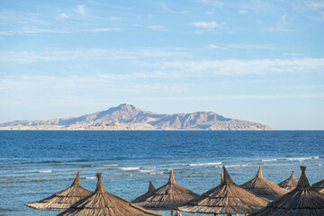 Aufkleber - Relaxing beach view with straw umbrellas and distant island in Egypt under clear sky