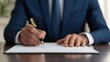 © OngCaLucK - A businessman in a suit writes on paper with a pen, emphasizing professionalism and attention to detail in a formal setting.