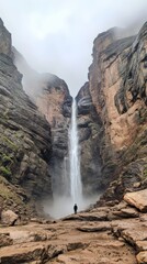 Poster - Lone hiker stands in awe at the base of a majestic waterfall, plummeting from towering cliffs shrouded in mist, creating a dramatic and serene landscape