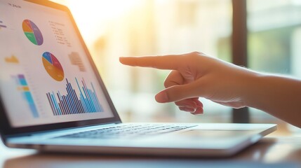 Aufkleber - Businesswoman pointing at financial charts displayed on a laptop screen, analyzing data for investment strategy and market trends in a bright office environment
